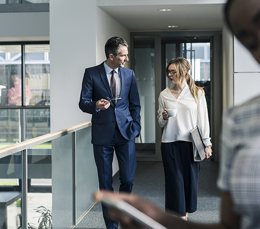 Image of two people walking down hallway in modern office building with lots of windows